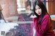 A woman in a red sweater leaning against a window.