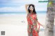 A woman in a red dress standing next to a palm tree on the beach.