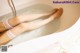 A woman is sitting in a bathtub with her legs in the water.