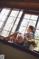 A woman sitting on a window sill with a vase of flowers.